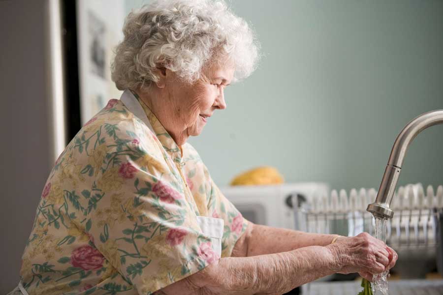 A elderly lady washing a vegetable at her sink in her home